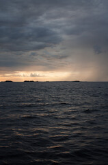 Naklejka na ściany i meble Sunset over the sea, with waves, stormy clouds and rain.