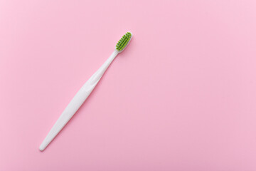 White plastic toothbrush with green bristle as flat lay. Toothbrush on pink surface, top view,...
