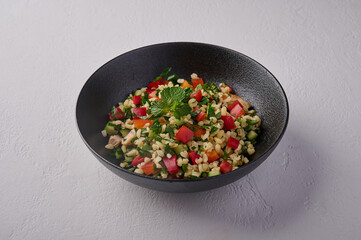 Middle Eastern traditional salad tabbouleh made of bulgur or couscous, poultry meat, parsley, mint, lemon, tomatoes and pepper, close up