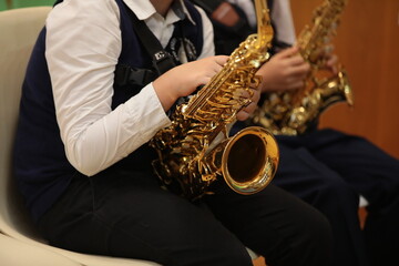 Obraz premium Children boys adolescents in the hands of a saxophone sitting on a chair inside the class at the lesson