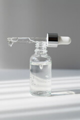 Opened facial serum in transparent bottle and dropper with drop on grey background with shadows. Liquid anti age treatment with vitamin C mockup. Natural cosmetic product closeup. Skin care concept.