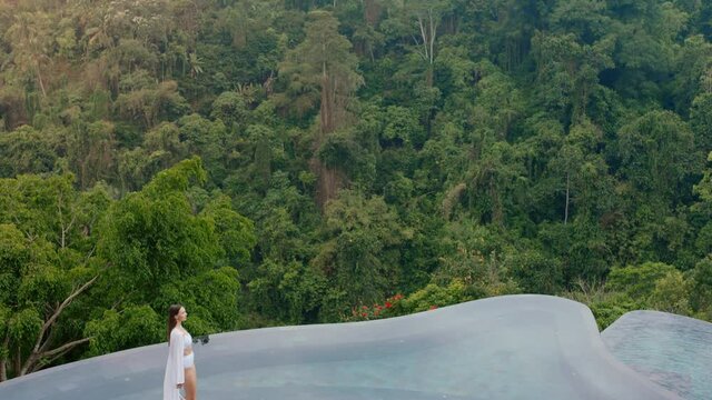 beautiful woman walking by infinity pool wearing bikini enjoying exotic summer vacation at luxury hotel spa with view of tropical jungle 4k