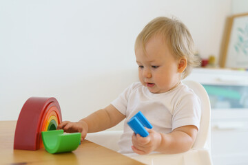 Blond blue-eyed curious caucasian baby playing and learning with plastic geometric figures. Concept of child motor development and leisure activity at kindergarten. Horizontal, copy space