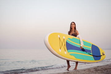 Young woman is carrying paddle board at the beach