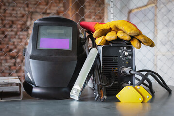 Welding inverter and welding mask on the metal workbench background. Front view.