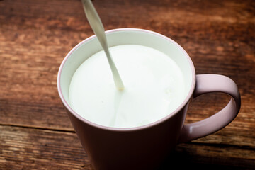 Milk is poured into a cup on a brown wooden background.