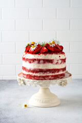 Red velvet cake with strawberry, whipped cream and bouquet of daisies on white board on gray...