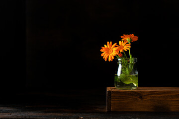 Calendula bouquet in a small vase on a black background.