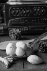 Shallow focus grayscale shot of peeled potatoes on a big ladle and ginger on a wooden table