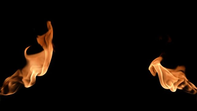 Two flames of fire blaze from different sides of screen in dark. Real bonfire, burner or torch flashes against black background. High speed flamethrower explodes with flame. Close up. Slow motion.