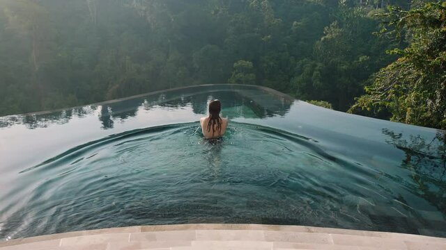 sexy woman swimming in infinity pool enjoying luxury lifestyle on exotic summer vacation at hotel spa with view of tropical jungle