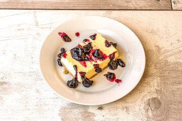 Rectangular portion of cheesecake with blueberry jam and compacted biscuit sand base on white plate
