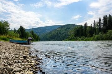 Fototapeta na wymiar Daytime landscape with a mountain river among coniferous forest with a motorboat on a rocky shore