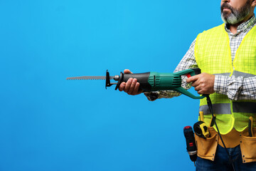 Handyman in uniform holding saw against blue background