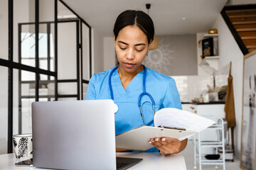 Black woman doctor working with laptop and papers at home