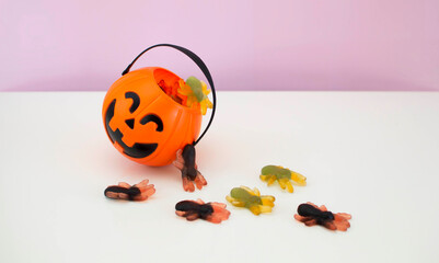 Sweets and sweets in a pumpkin bucket on an orange background. Halloween decor: a pumpkin basket...
