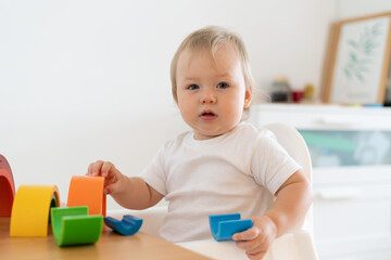 Adorable caucasian blond blue-eyed child playing and learning with wooden bricks and blocks. Concept of child development and education at home. Horizontal, copy space