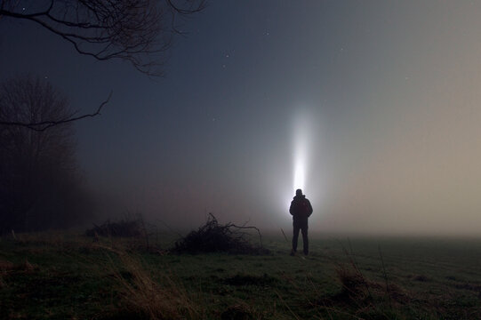 An Atmospheric, Moody Concept. Of A Man With A Torch Looking At The Sky, In A Field On A Misty Winters Night. UK.