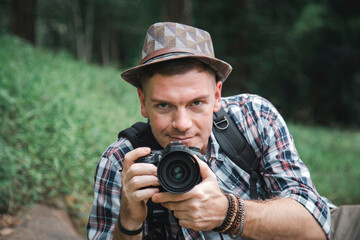 Young caucasian tourist man smiling and holding dslr camera in nature background.