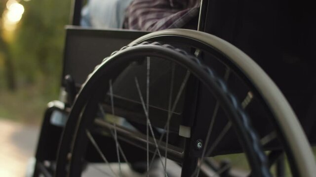 Moving wheel of wheelchair closeup. Woman is pushing disabled person in wheelchair. Concept of serious diagnosis and paralysis