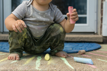 Toddler squatting while playing with chalk on the front steps of her house: child wearing camouflage print pants and star print top