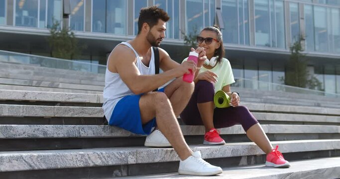 Fit diverse couple taking rest after workout outdoors, sitting on urban stairs
