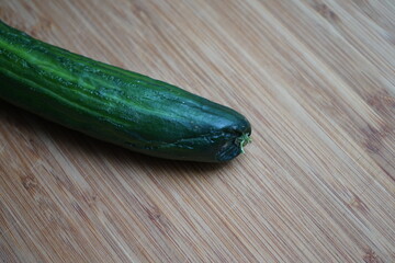 A slim not too fresh cucumber lies on a wooden board
