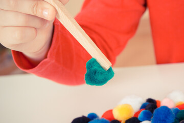 Preschooler playing with small pompoms and wooden tongs. Development of kids motor skills, coordination and logical thinking