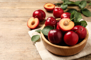 Delicious ripe cherry plums with leaves on wooden table. Space for text