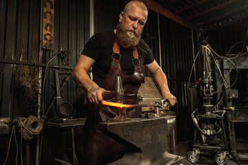 Fototapeta na wymiar Bearded man, blacksmith manually forging the molten metal on the anvil in smithy with spark fireworks. Concept of labor, retro professions, family business