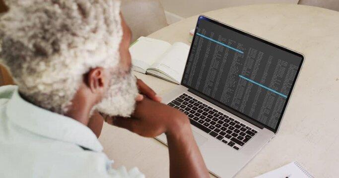 African american man sitting at desk watching coding data processing on laptop screen