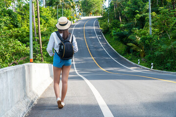 Adventure recreation and travel transport concept. Young woman wearing hat carrying backpack while walking alone on the roadside highway looking someting.