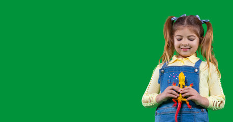 Beautiful smiling little girl holding a dinosaur toy yellow color in her hands and is looking at it.