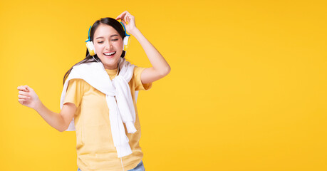Cheerful enjoy young woman wearing headphones listening to music form smartphone and dancing relax over isolated yellow background. Lifestyle leisure with hobby concept.