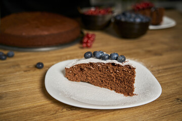 A woman with a passion for cooking decorates a slice of handmade chocolate cake in her home kitchen with blackberries, red currants and a sweet white rain of powdered sugar.