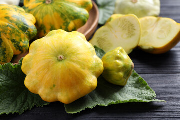 Fresh ripe yellow pattypan squashes with leaves on black wooden table, closeup