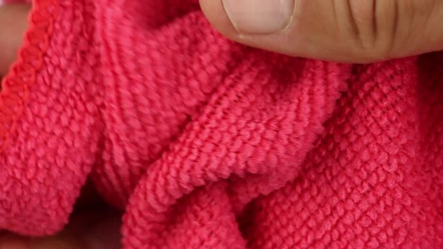 hands testing, crushes and stretches red microfiber dusting cloth, well-absorbing water synthetic fabric, close-up view on texture of textile