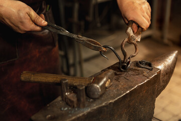 Close-up working powerful hands of male blacksmith forge an iron product in a blacksmith. Hammer,...