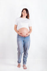 Pregnant woman caressing her belly over white background. Full-length portrait of the expectant mother on a white background