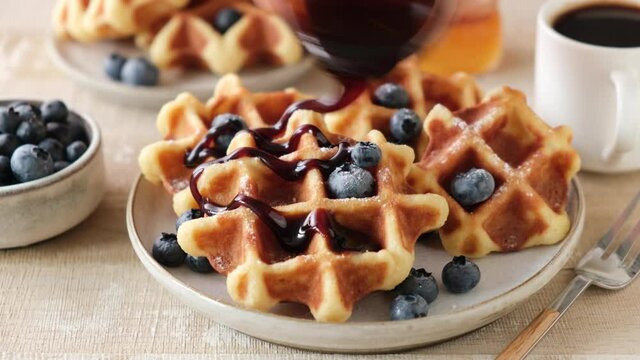 Pouring molasses or dark amber maple syrup on belgian waffles. Sweet breakfast food