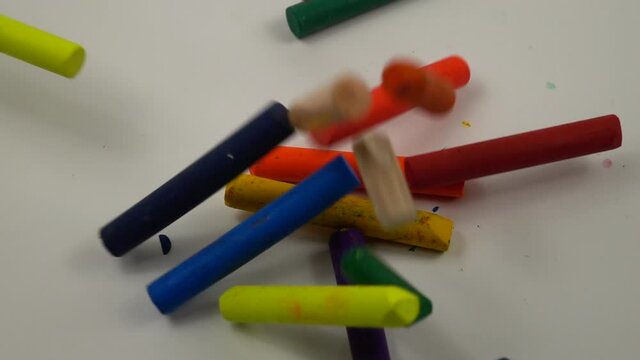 Sticks of multicolored wax crayons fall on a white table, slow motion. Colorful wax crayons scattered on a white table.
