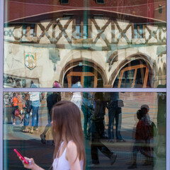 A girl with a phone and reflecting people in the glass on the street.