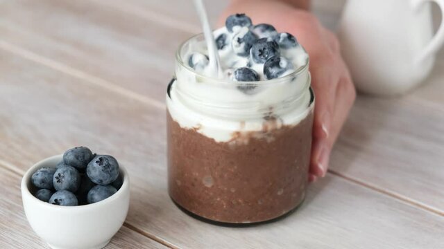 Eating chocolate chia pudding with greek yogurt and blueberries with spoon. Healthy low carb sugar free dessert