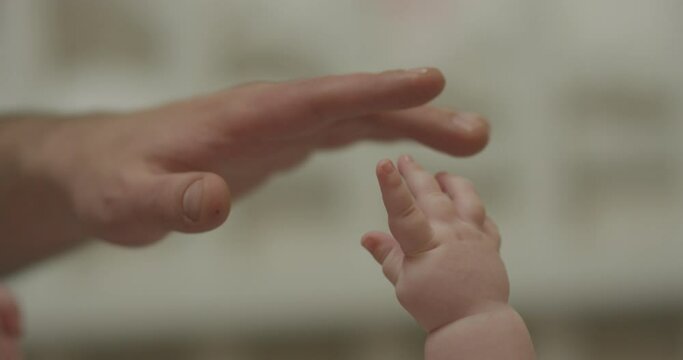 4K Closeup shot of baby's little cute hand reaching for father's loving finger . Baby holding parent's finger. Parent holding newborns hand in Slow Motion. Hand in hand. Father and newborn baby . 