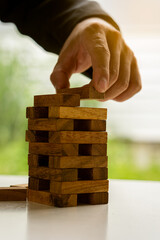 Planning, Risk and Strategies A businessman puts a wooden block on a tower on an office table.