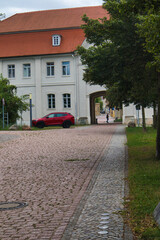 Obraz premium Gepflasterte Zufahrt und historischer Torbogen am Schloss mit modernem roten Fahrzeug und typischer Architektur, Köthen, Landkreis Anhalt-Bitterfeld, Sachsen-Anhalt, Deutschland
