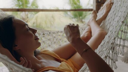 happy woman in hammock enjoying comfortable lifestyle on holiday in vacation resort swaying peacefully on lazy summer day in tropical paradise cabin
