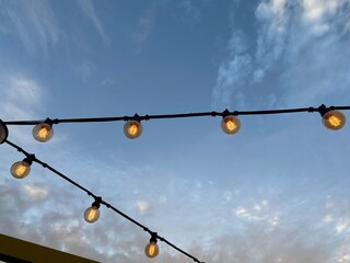 Hanging light bulbs against the background of the evening sky in a summer cafe 