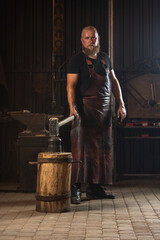 Full ength portrait of bearded man, blacksmith working on creating handmade metal product at family...