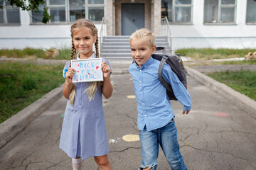 Elementary school kids. Happy girl holds picture with back to school message and boy with backpack...